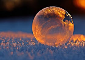 pexels-photo-302743-302743-1 Close-up shot of a frozen bubble with warm reflections resting on a snowy surface at twilight.